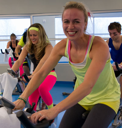 LECOM female student in yellow tank top on bike in LECOM Fitness Center