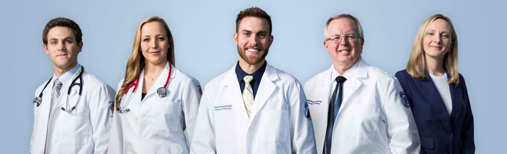 Two male students in white coats, one female student in white coat, one male doctor in white coat and one female in navy suit at LECOM