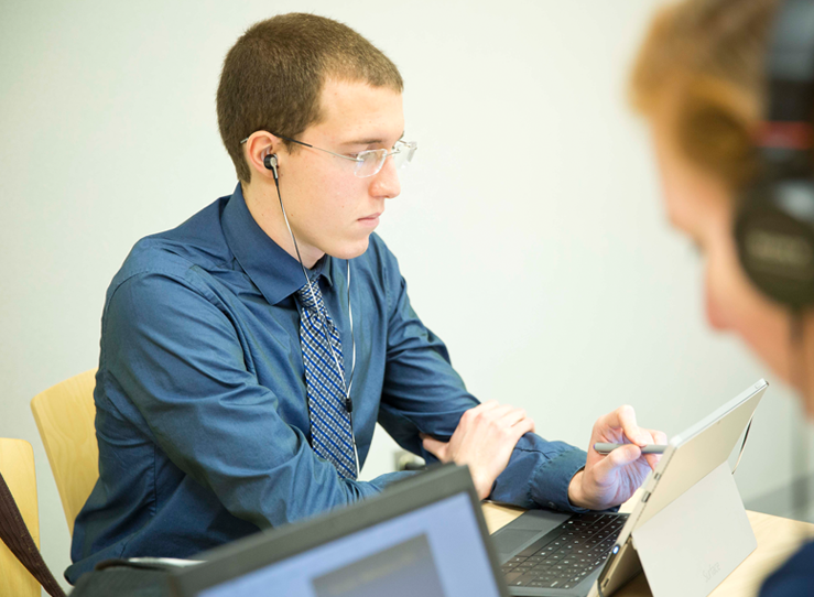 Student with headphones looking at tablet in library at LECOM