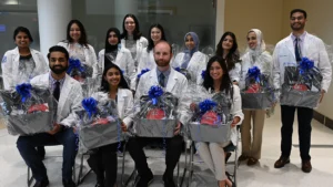 LECOM Students holding baskets while sitting in chairs in their white coats.